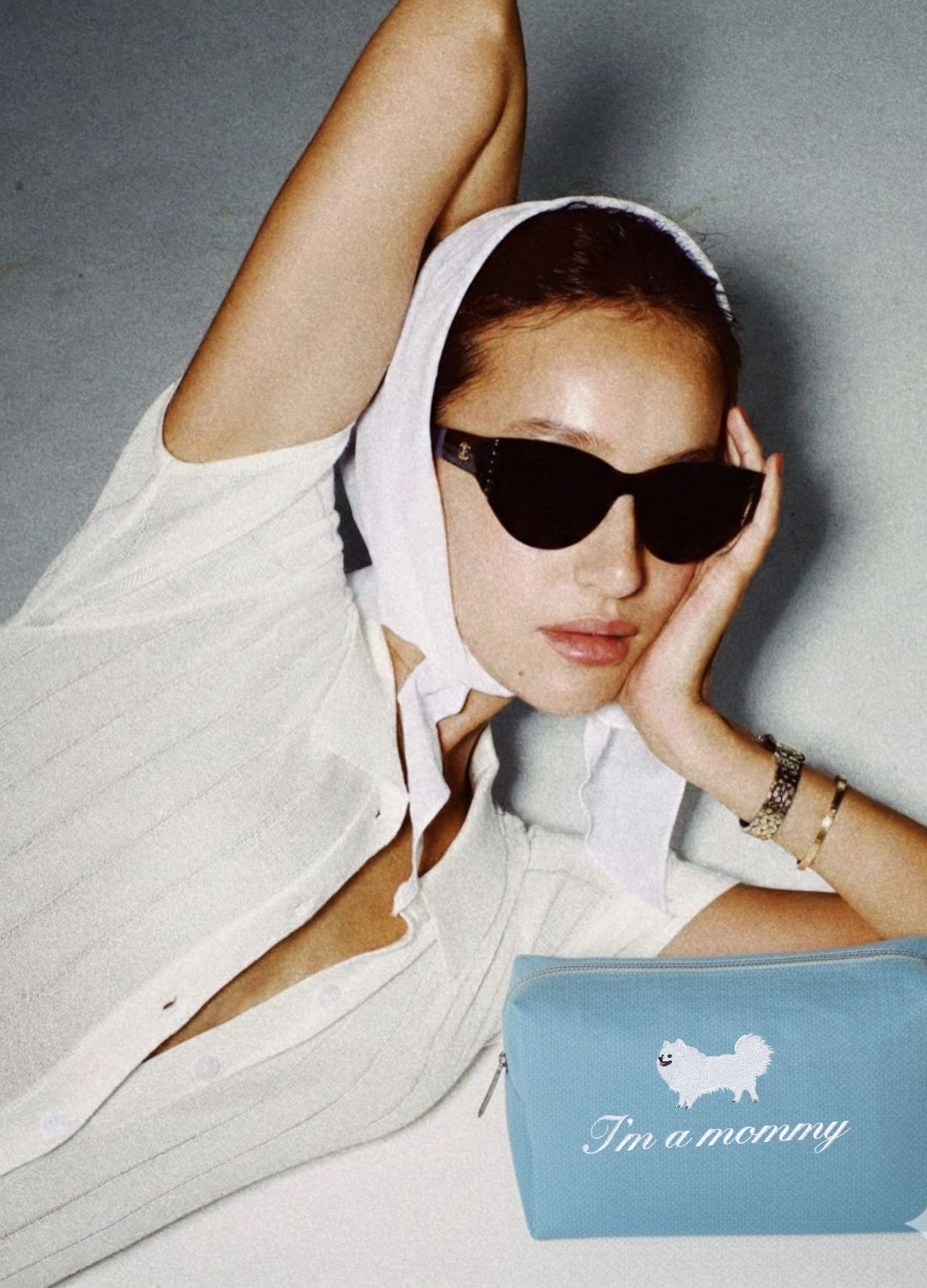 Woman wearing sunglasses and a white headscarf with a blue pouch labeled 'I'm a mommy' on a gray background