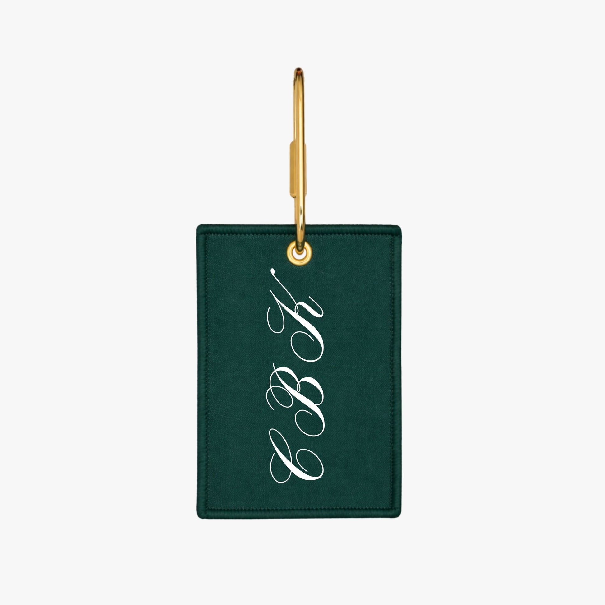Green luggage tag with gold hook and white monogram on a white background