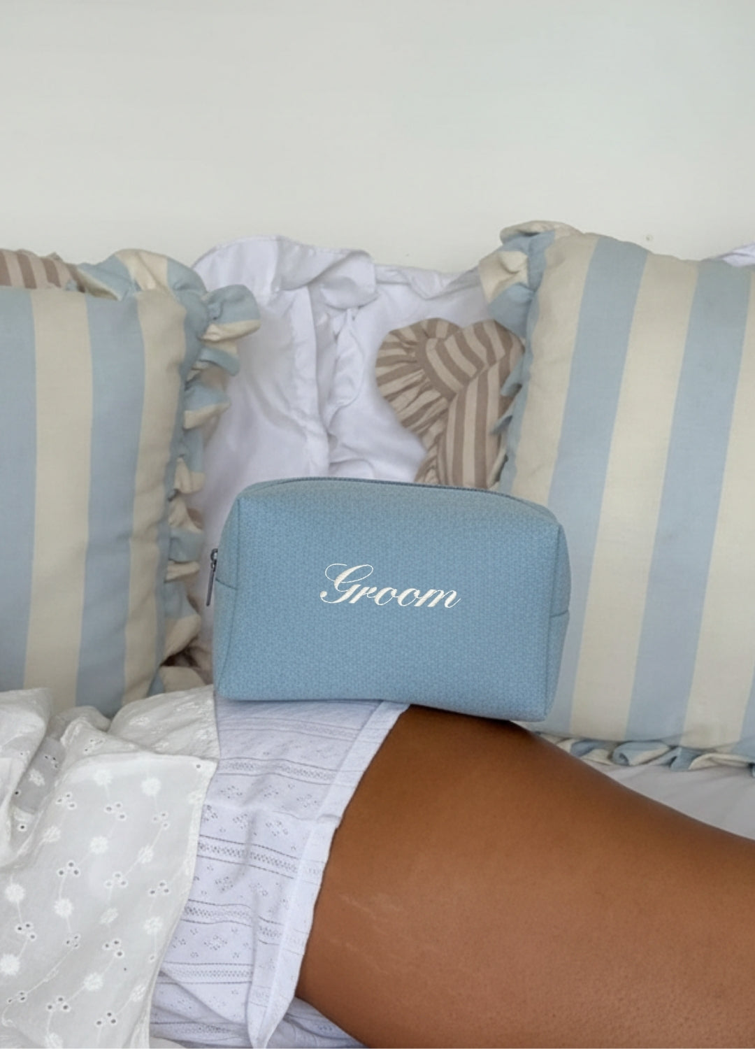 Blue pouch labeled 'Groom' on a bed with striped pillows