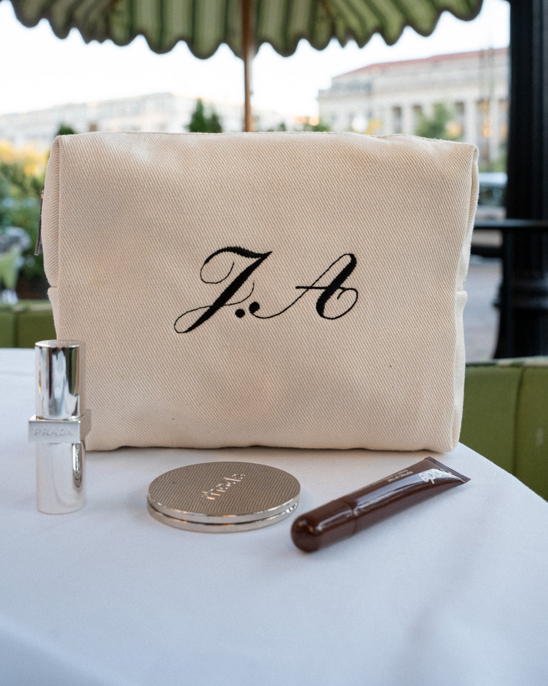 Beige pouch with 'F.A' monogram on a table with rhode gloss and rhode mirror